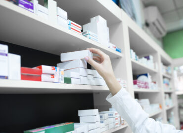 Closeup view of pharmacist hand taking medicine box from the shelf in drug store.